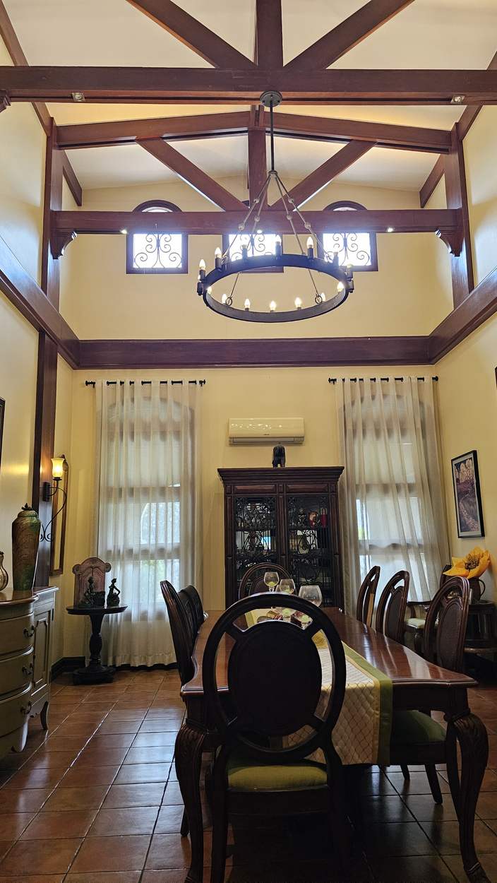 Luxury dining room with vaulted ceiling, exposed solid wood beams, clerestory windows and a wrought-iron chandelier