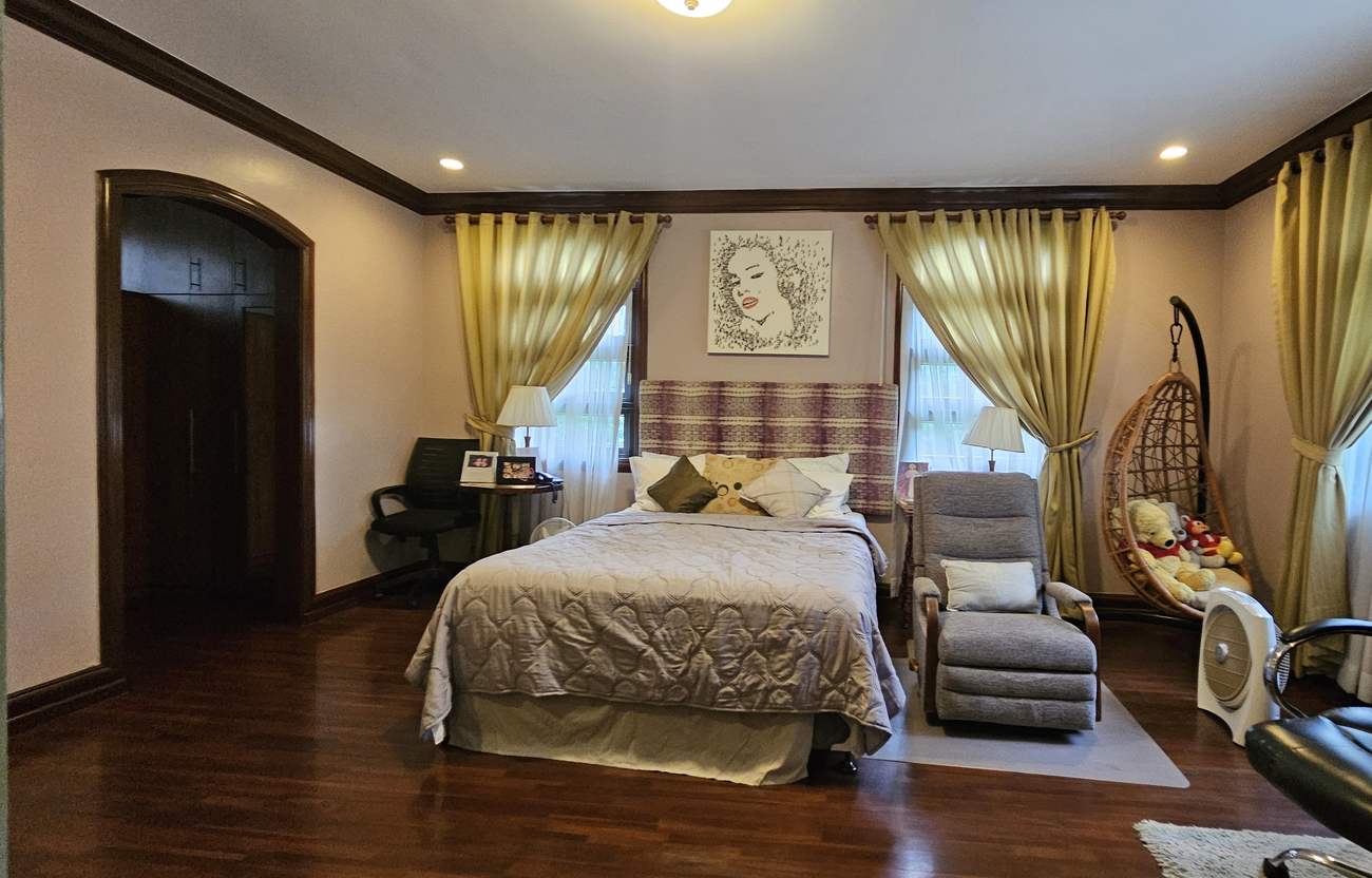 Master bedroom retreat with hardwood flooring, tall curtained windows and arched entry to the walk-in closet